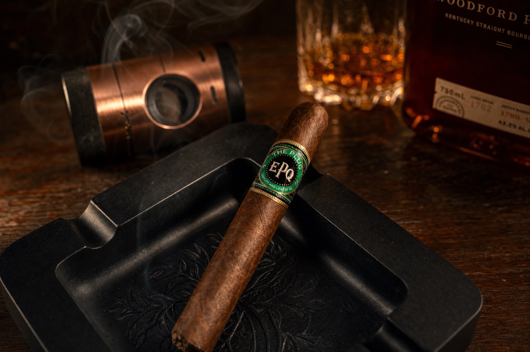 The Plug on a black ashtray with a copper cutter and bourbon in the background